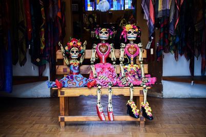 three day of the dead skeletons sitting on a park bench indoors