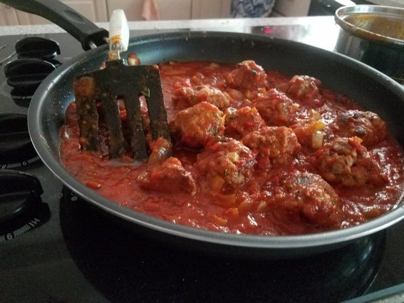 herb meatballs sizzling in a saute pan with tomato sauce